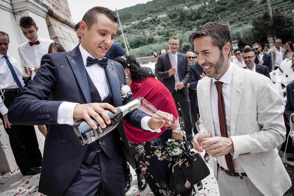 sposo che versa il vino per il brindisi davanti alla chiesa di Monte in valpolicella